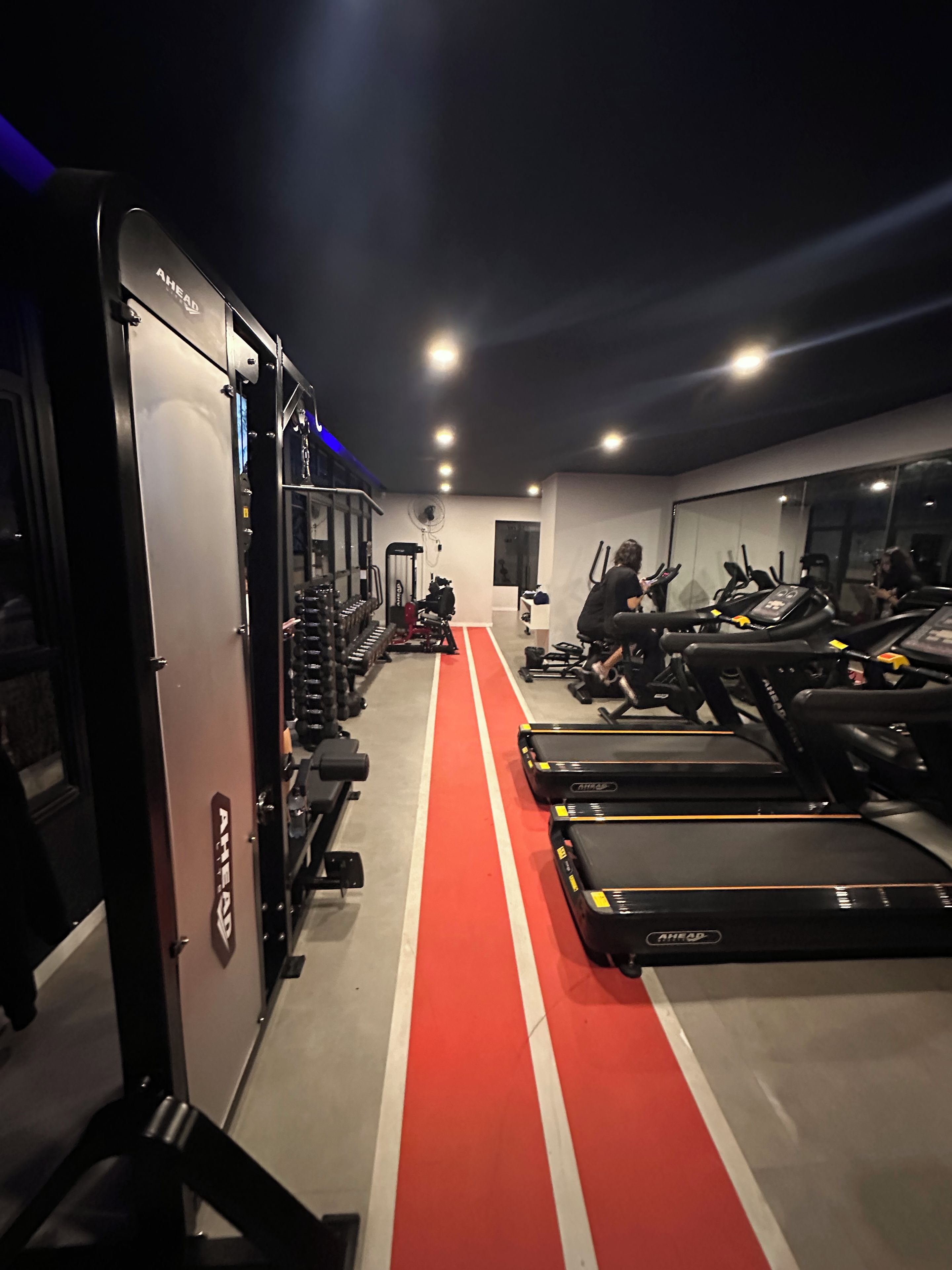 A gym with treadmills, weight machines, and a red running track.