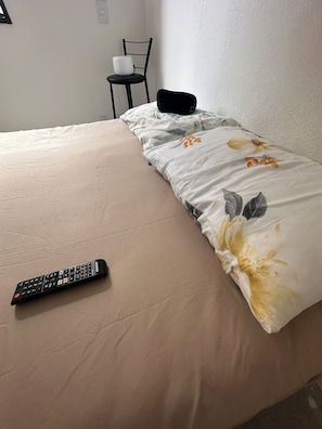 A bed with a floral comforter, a remote control on the bed, and a chair in the background. - Luxury Apartment in Alphaville Barueri (Barueri)