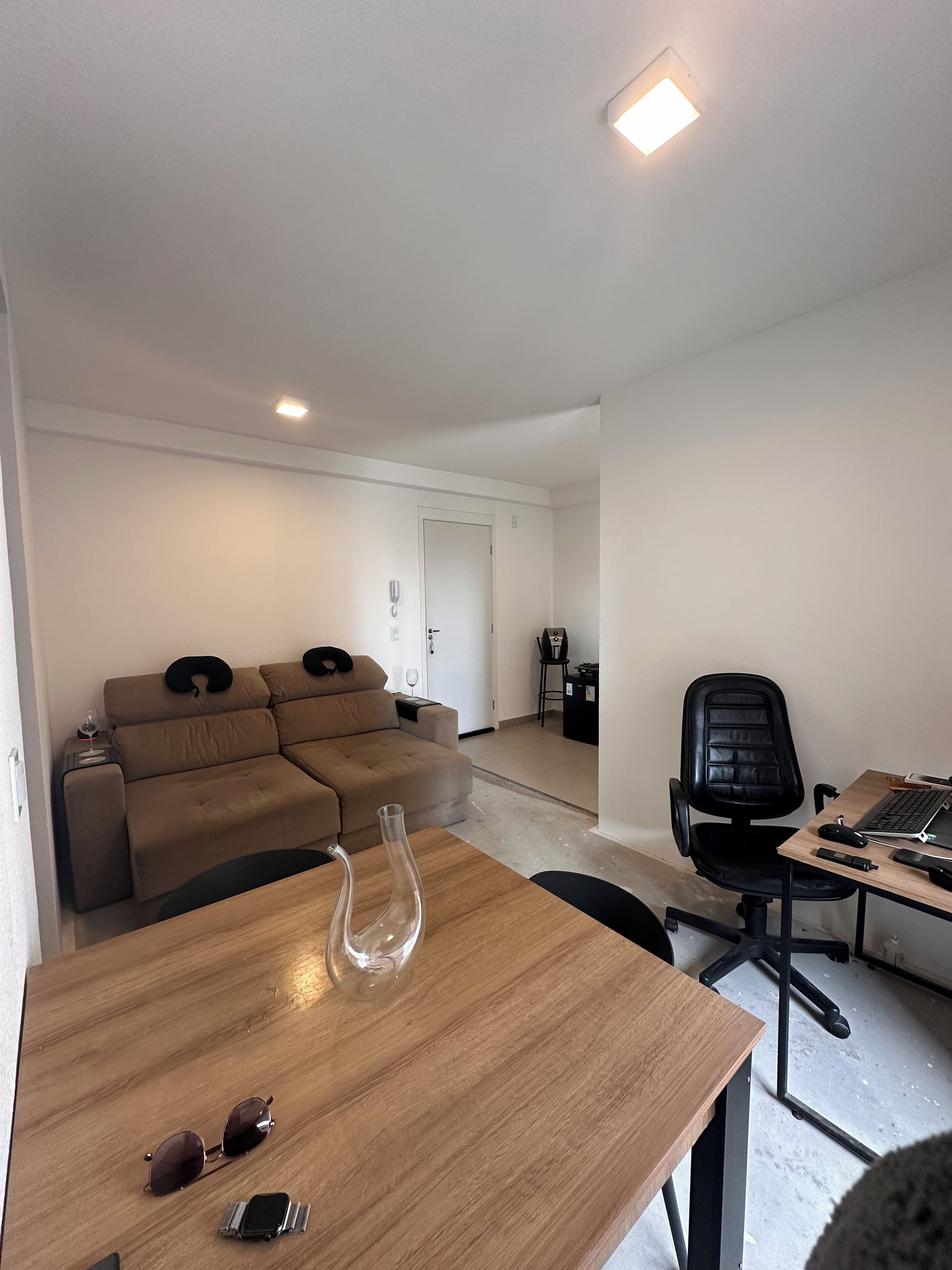 A modern living room with a sofa, a dining table, and a workspace with a chair and laptop.
