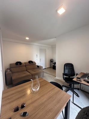 A modern living room with a sofa, a dining table, and a workspace with a chair and laptop. - Luxury Apartment in Alphaville Barueri (Barueri)