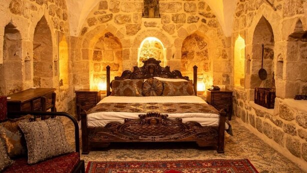 A stone-walled room with a large bed, a wooden headboard, and a carpeted floor. - Katmani Hotel (ARTUKLU)