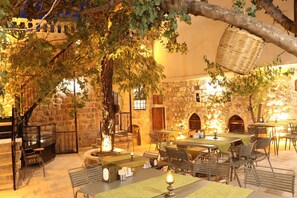 An outdoor dining area with stone walls, wooden furniture, and a fire pit. - Katmani Hotel (ARTUKLU)