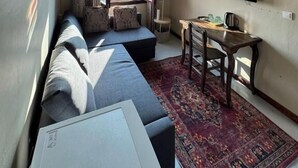 Un espacio habitable compacto con un sofá, una mesita, un televisor montado en la pared y una ventana con cortinas.