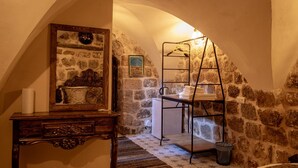 Una habitación rústica con pared de piedra, cómoda de madera, tendedero de metal y suelo de baldosas.
