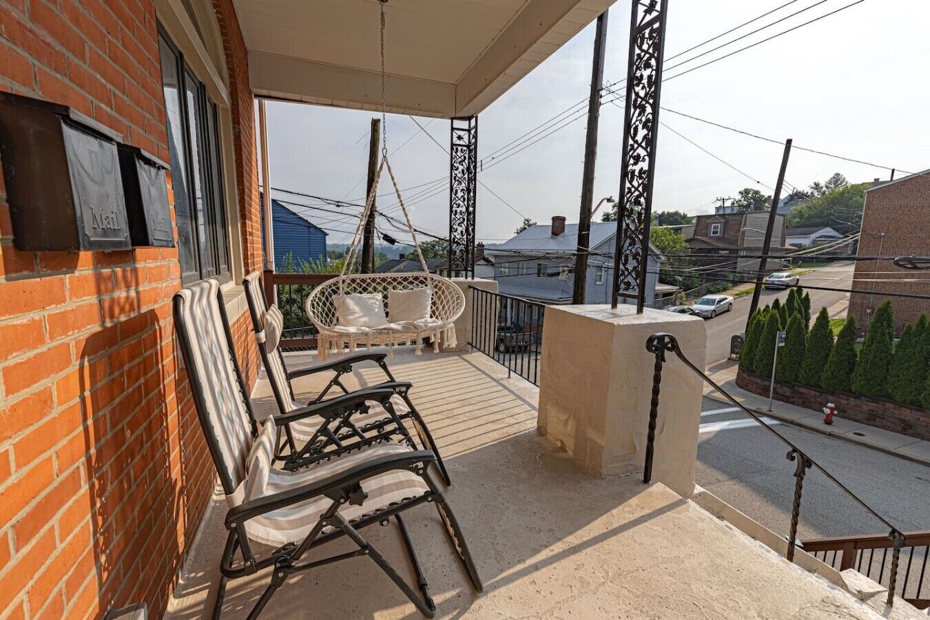 Een balkon met een schommelstoel en een zachte bank, een bakstenen muur en uitzicht op de straat.