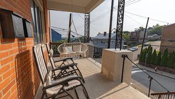 Een balkon met een schommelstoel en een zachte bank, een bakstenen muur en uitzicht op de straat.