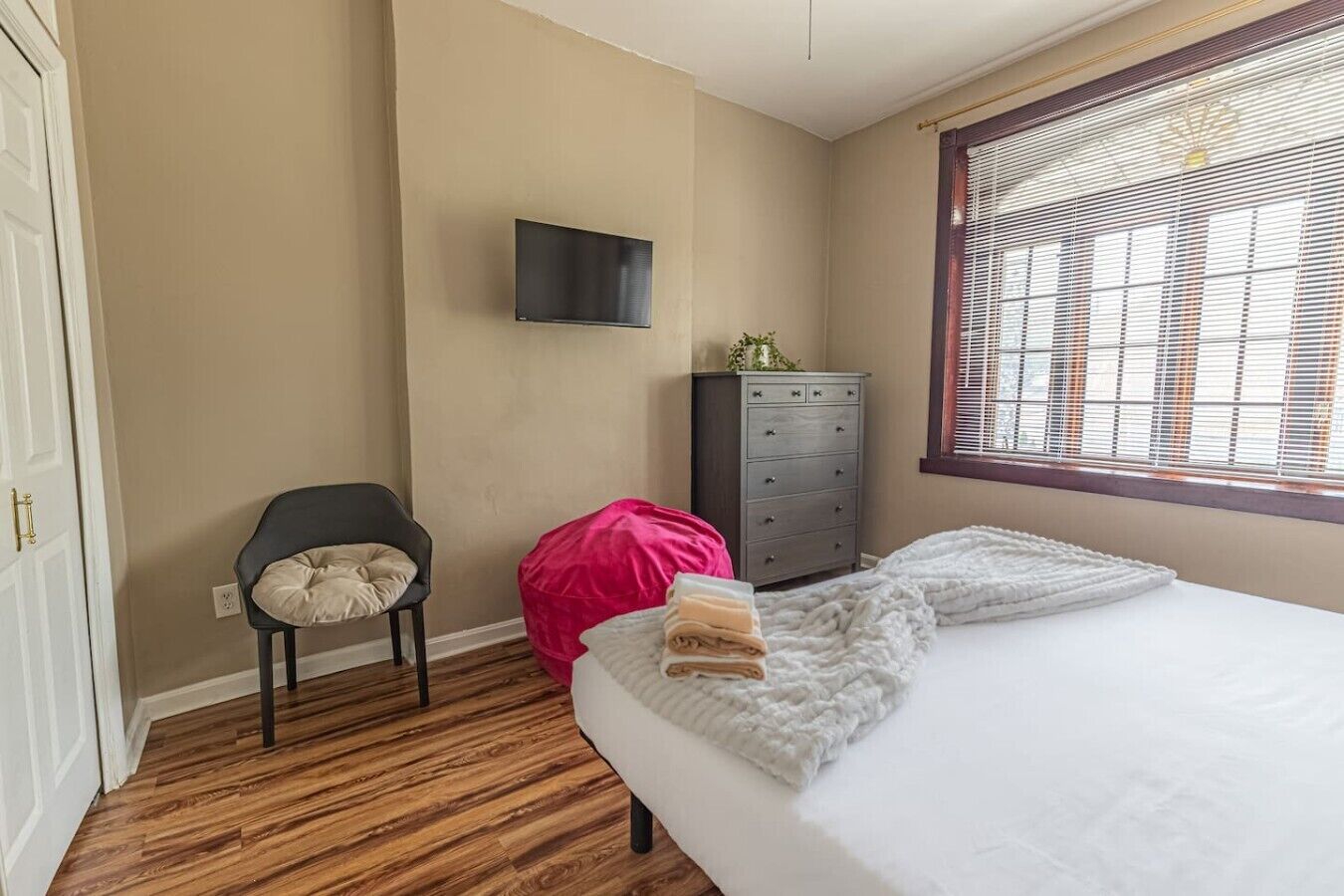 Een slaapkamer met een bed, een stoel, een dressoir en een televisie aan de muur.