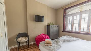 Een slaapkamer met een bed, een stoel, een dressoir en een televisie aan de muur.
