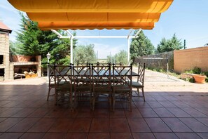Een overdekte patio met een tafel en stoelen, omringd door een bakstenen muur en groen.