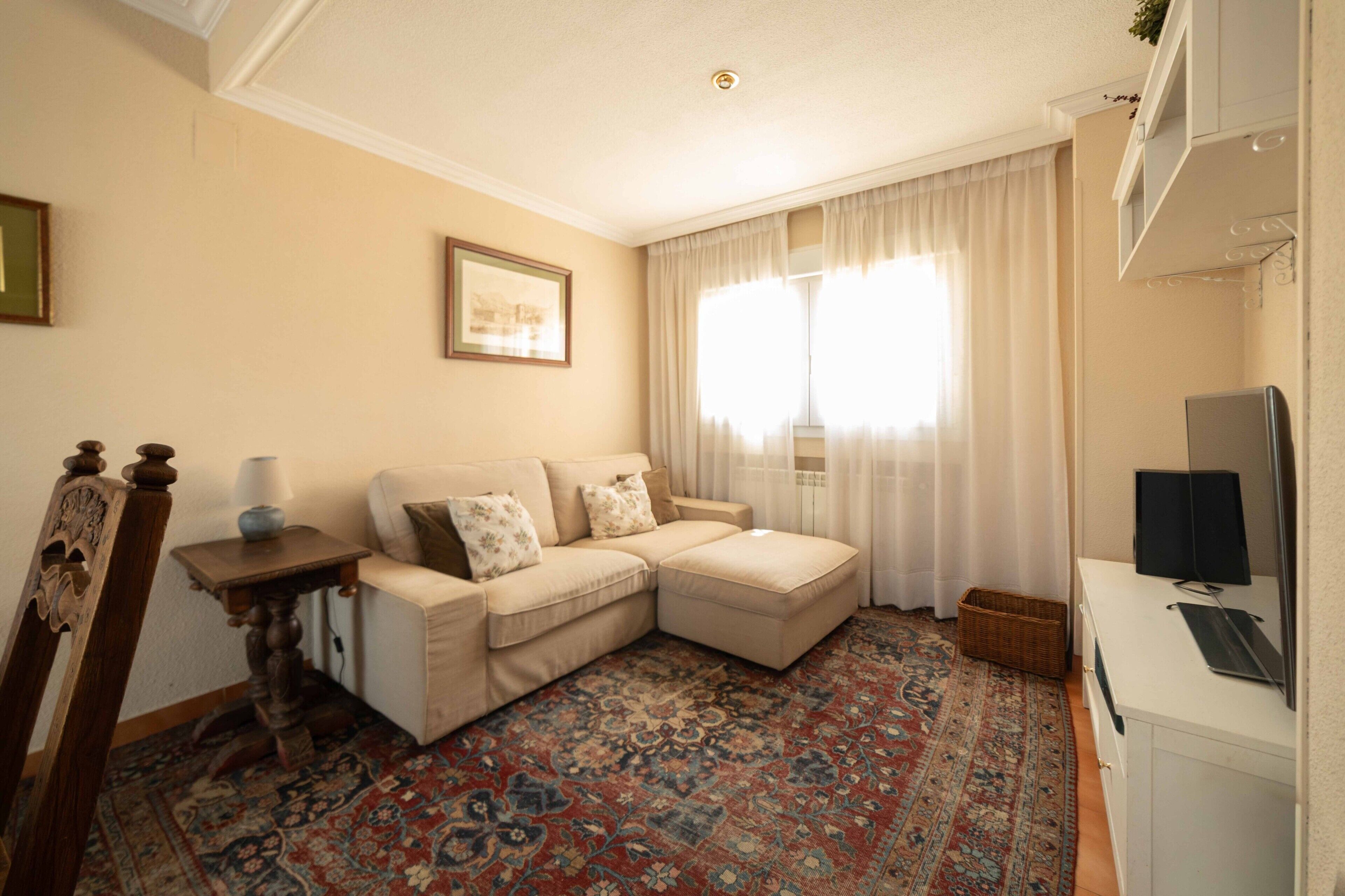 Een woonkamer met een beige bank, een kamerbreed tapijt, een televisie en een lijst met een foto aan de muur.