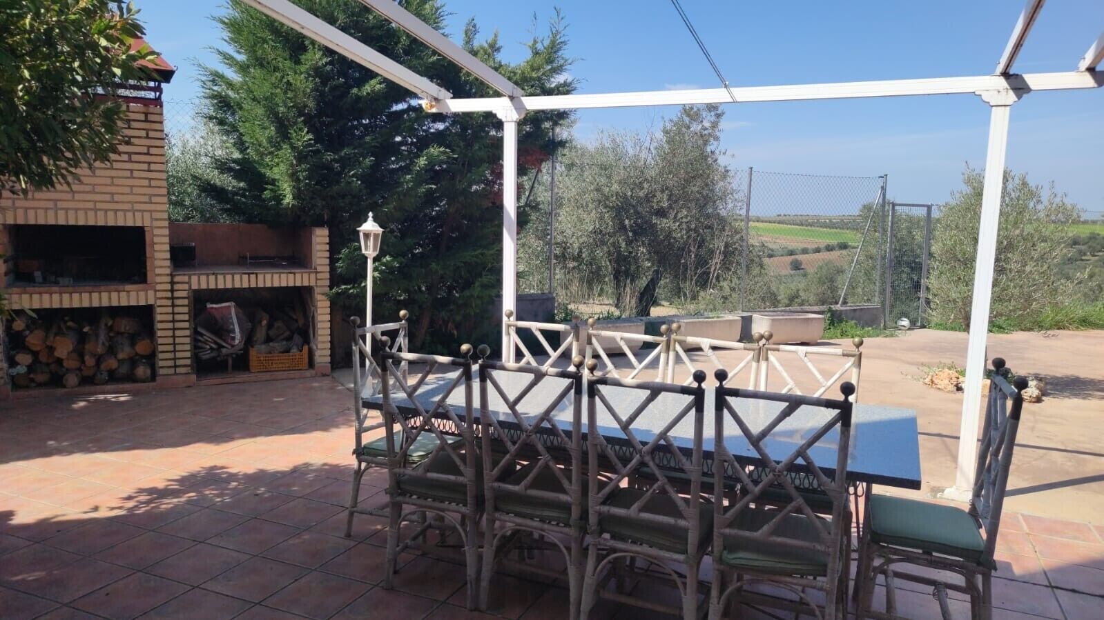 Een terras buiten met een tafel en stoelen, omgeven door een witte pergola.