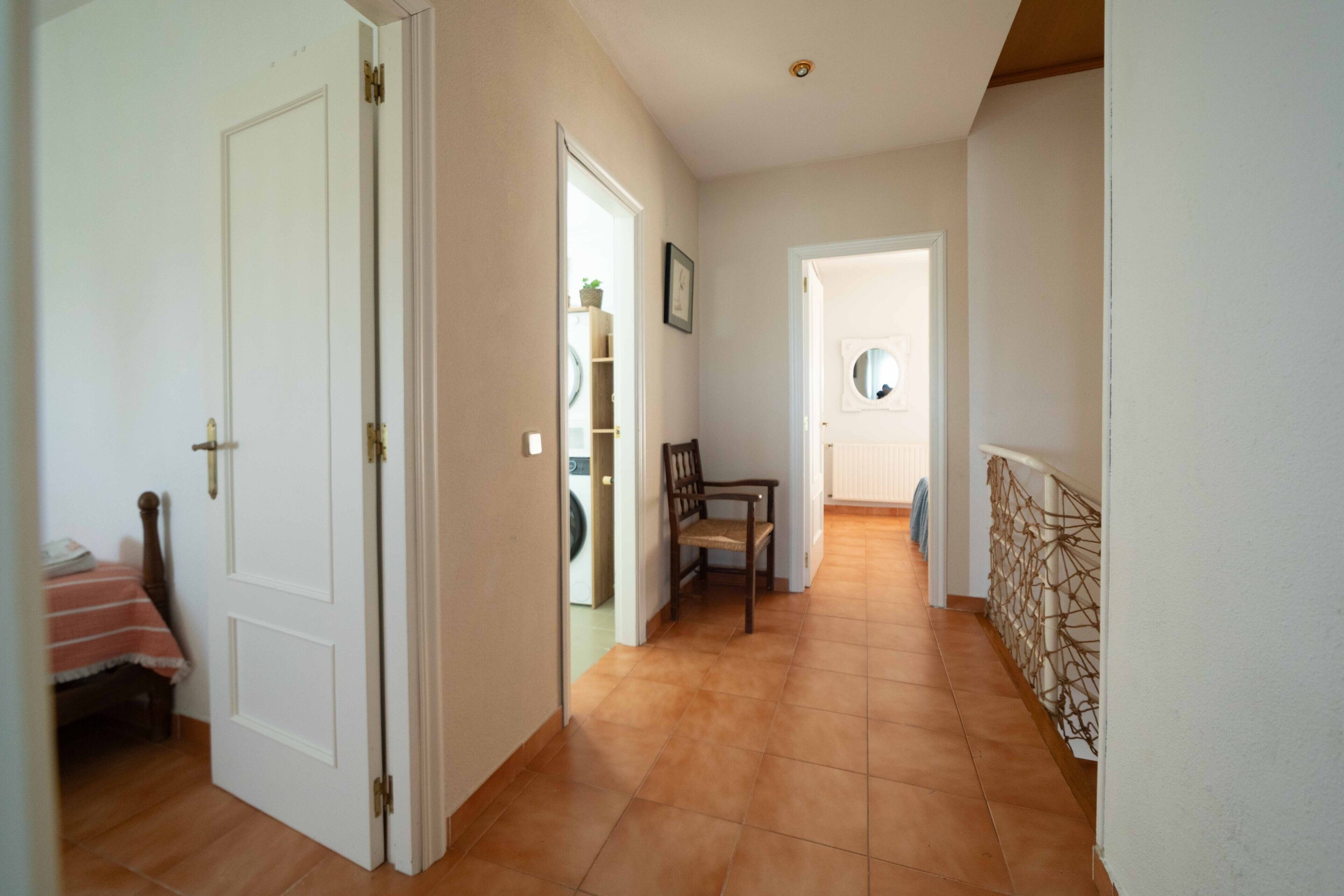 Un pasillo con una puerta de madera, una silla y una mesita con mantel rojo.