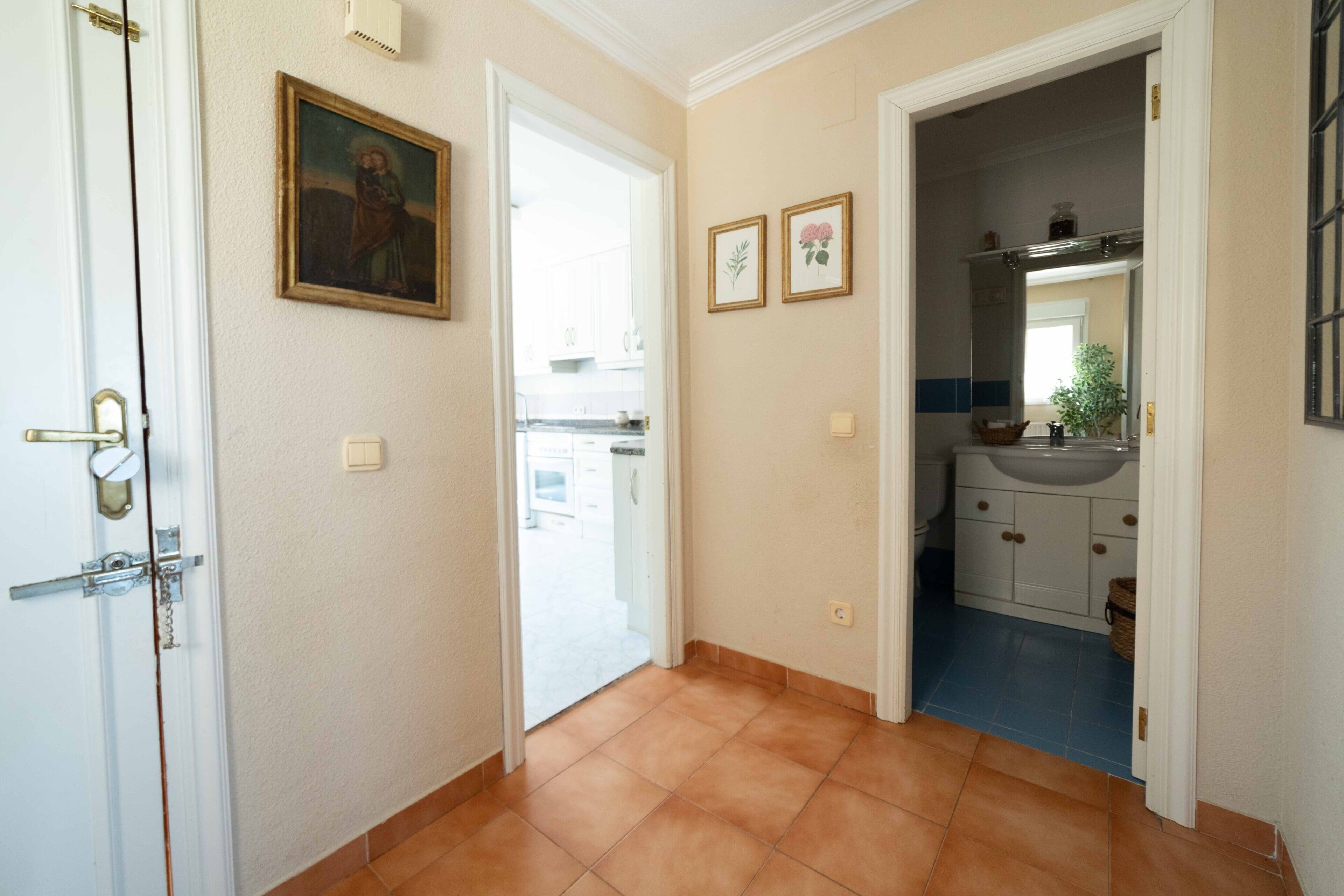 Een gang met een deur naar een badkamer, een schilderij aan de muur en een betegelde vloer.