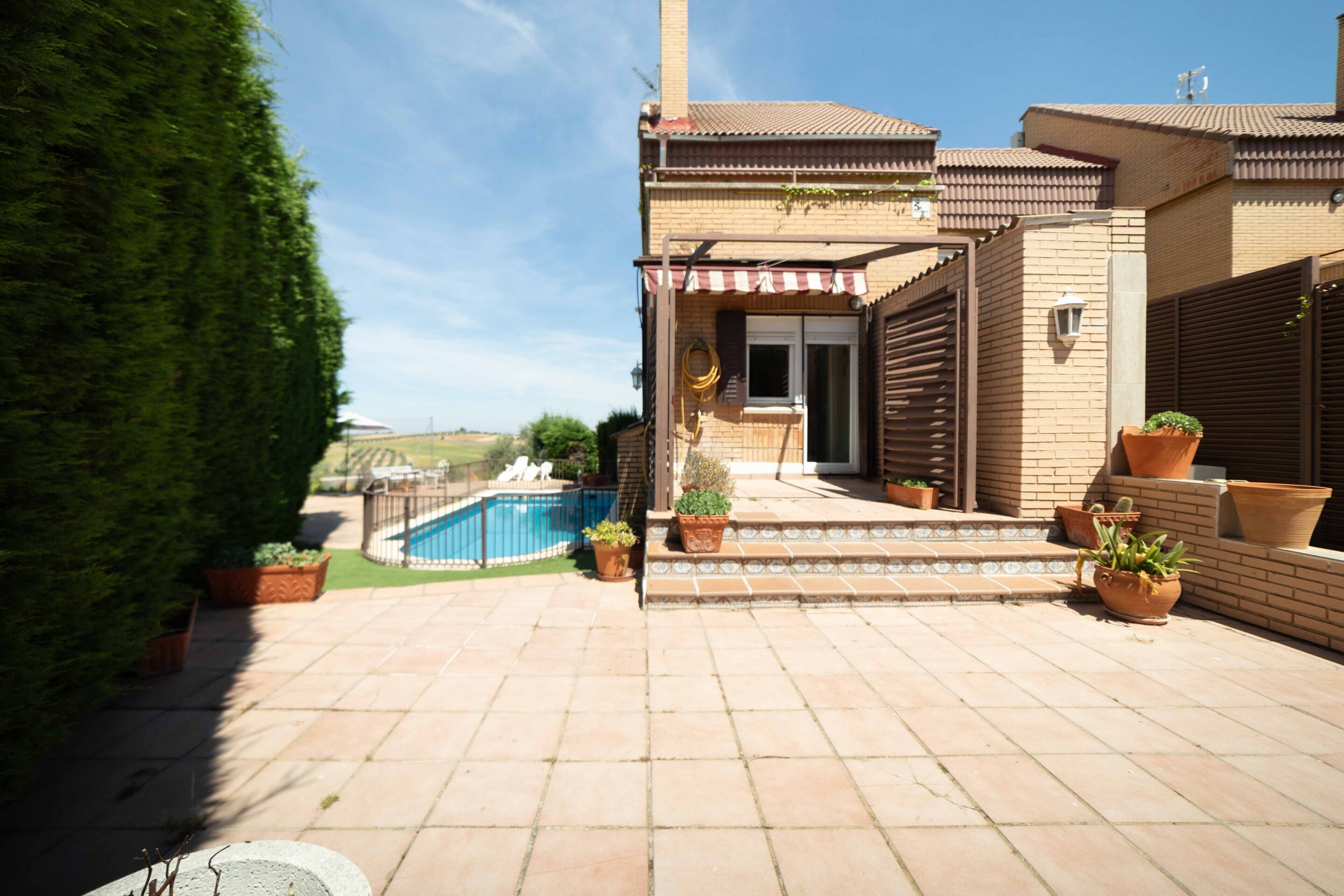 Une propriété résidentielle dotée d’une piscine, de plantes en pot et d’une terrasse carrelée.