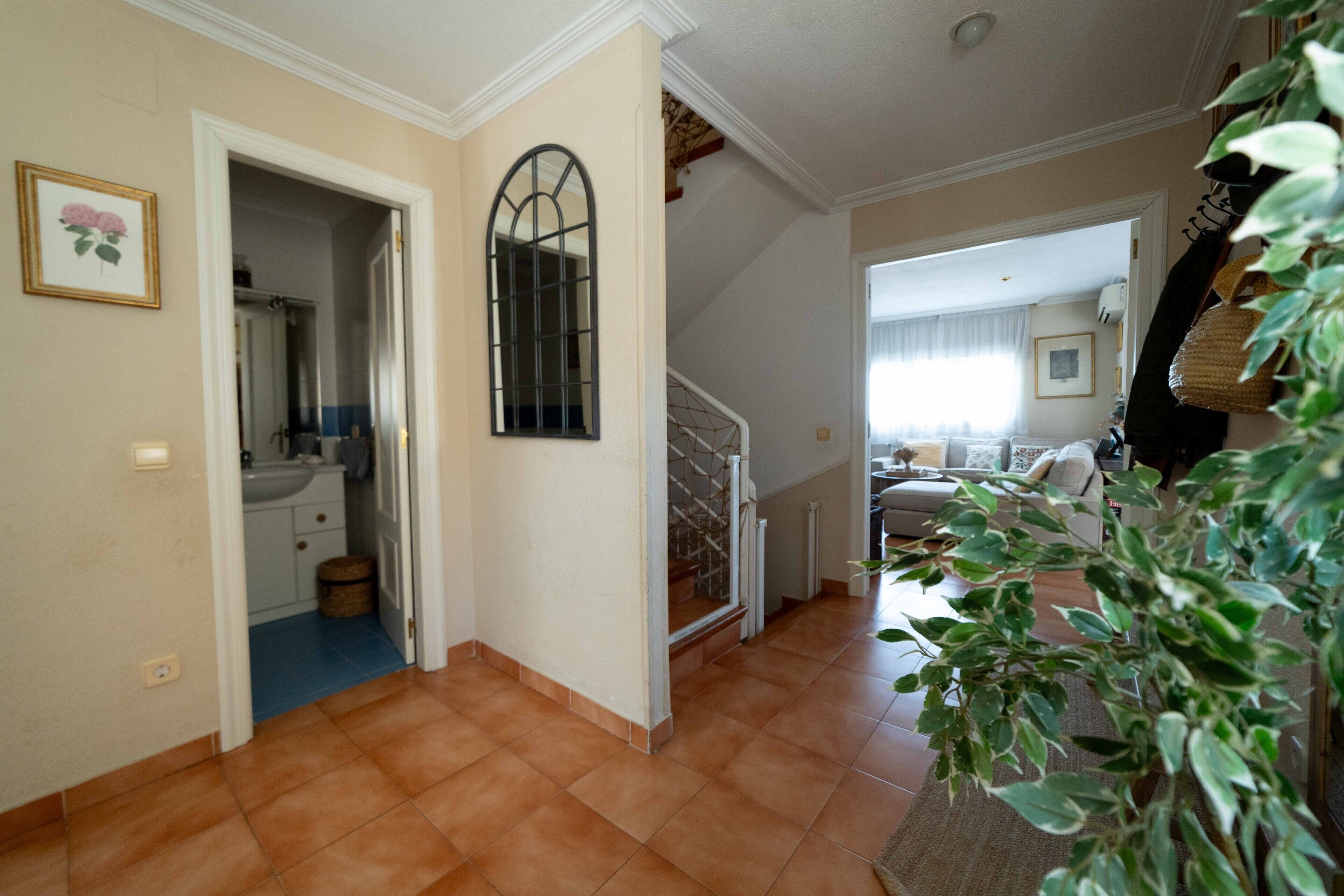 Un pasillo con un baño, una escalera y una sala de estar con sofá y una planta.
