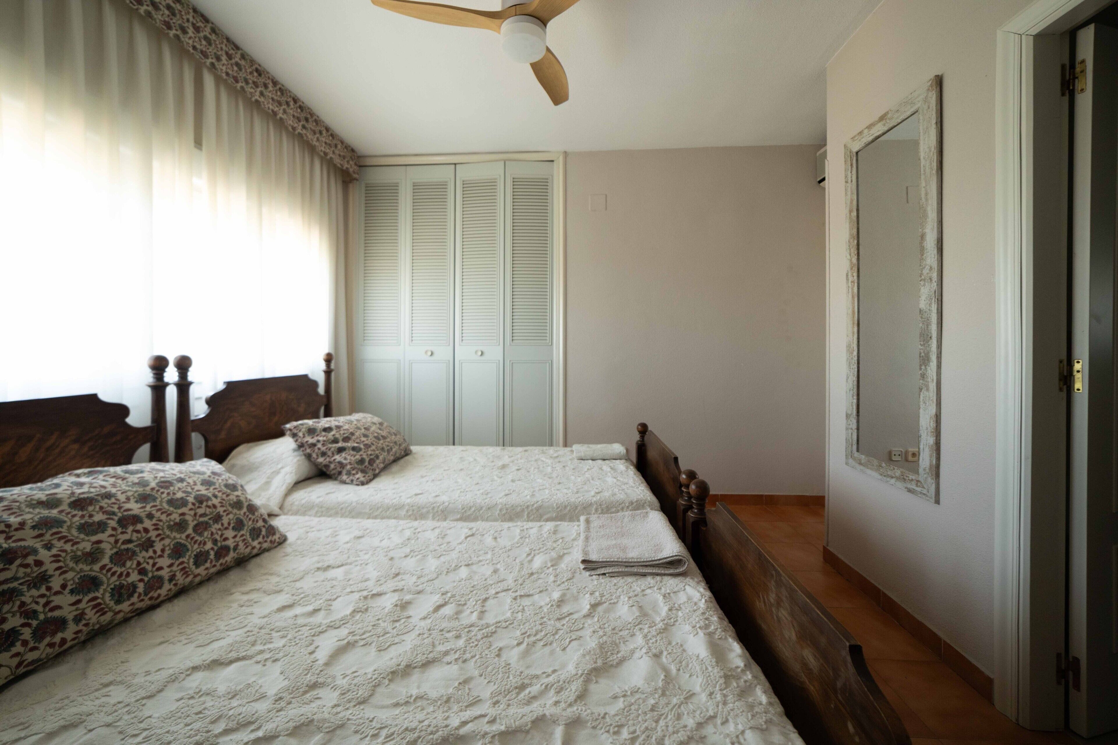 A bedroom with two beds, a ceiling fan, a wardrobe, and a door.