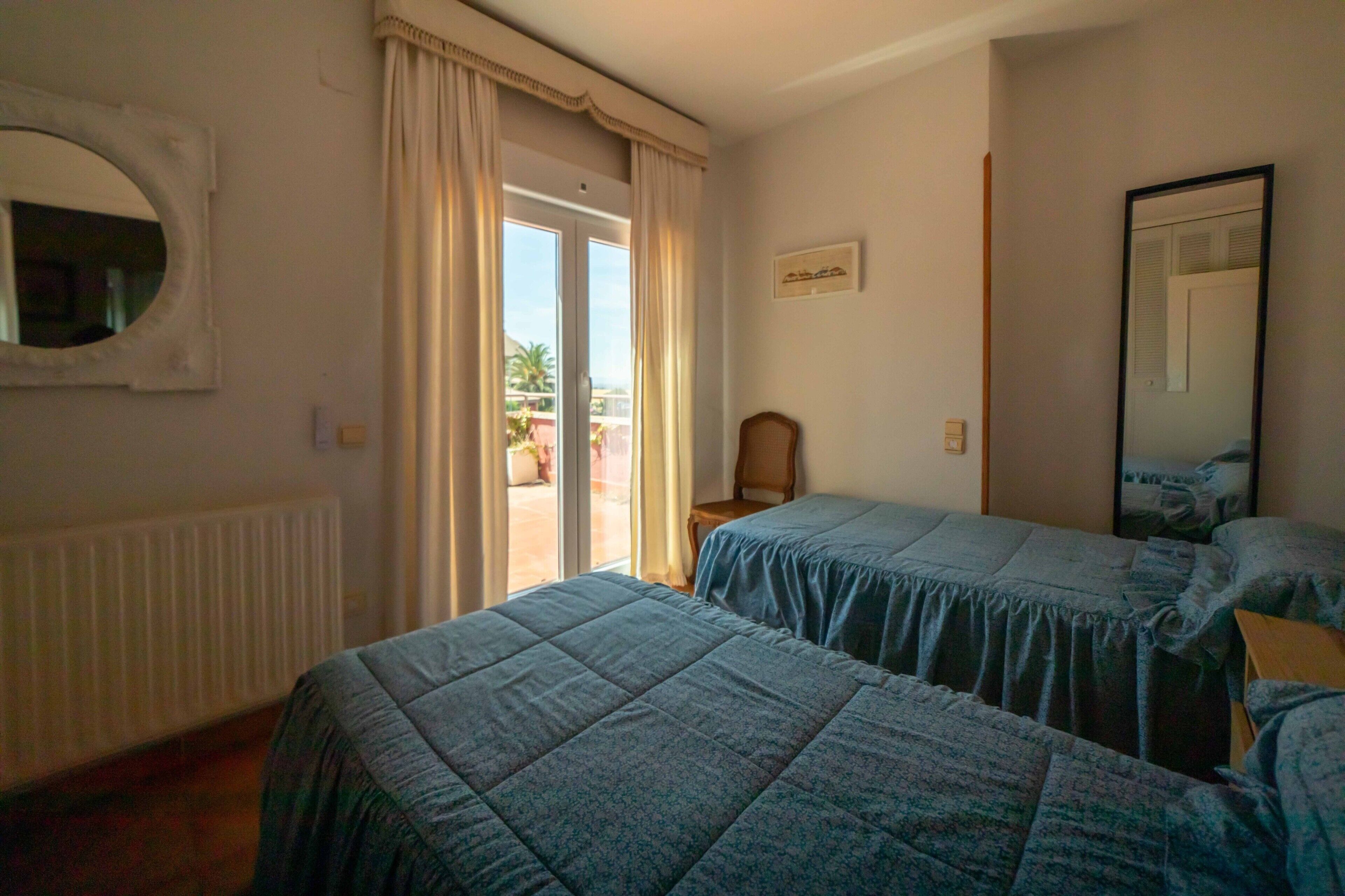 Habitación de hotel con dos camas, una ventana con cortinas, un radiador, una silla y un espejo.