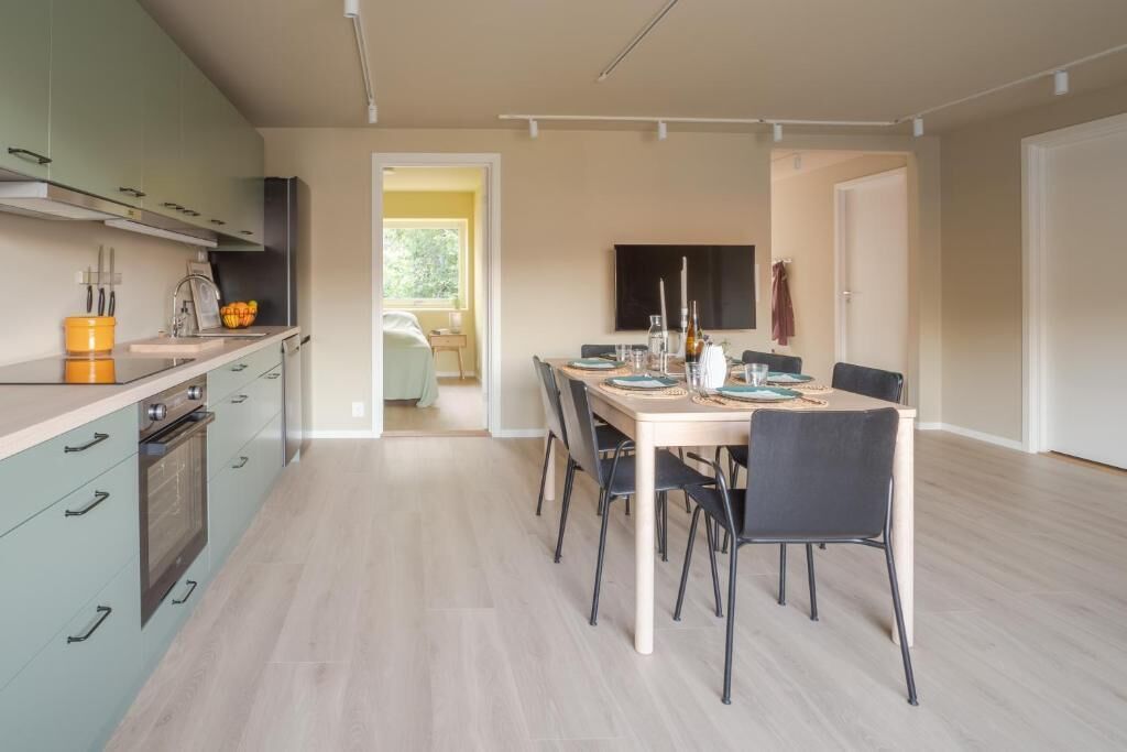 A modern kitchen with a dining area, featuring a large table and chairs, a built-in oven, and a view into the adjacent living space.