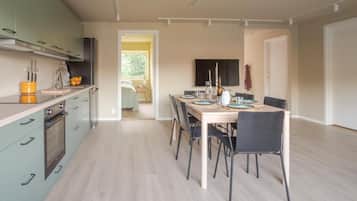 A modern kitchen with a dining area, featuring a large table and chairs, a built-in oven, and a view into the adjacent living space.