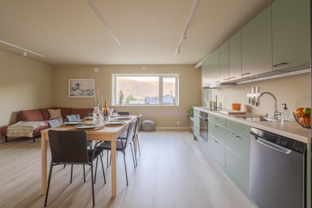 A modern kitchen with a dining area, a sofa, and a large window.