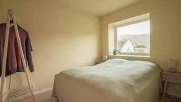 A bedroom with a bed, a window, a nightstand, and a drying rack.