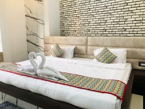 A neatly made bed with white linens and decorative pillows, a headboard with a brick pattern, and a wall with a marble-like design. - jss .inn pushkar (Ajmer)