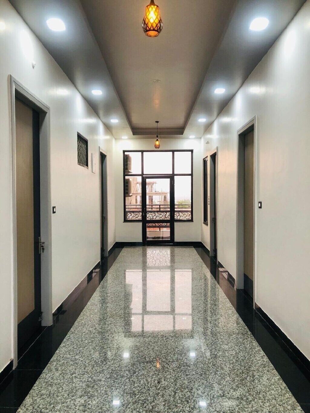 A hallway with a polished floor, doors on both sides, and a large window at the end.