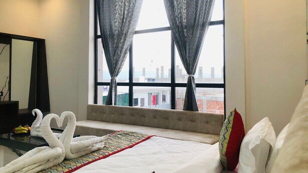 Habitación de hotel con cama, vistas a la ciudad a través de amplios ventanales y una decoración de toallas con forma de cisne.