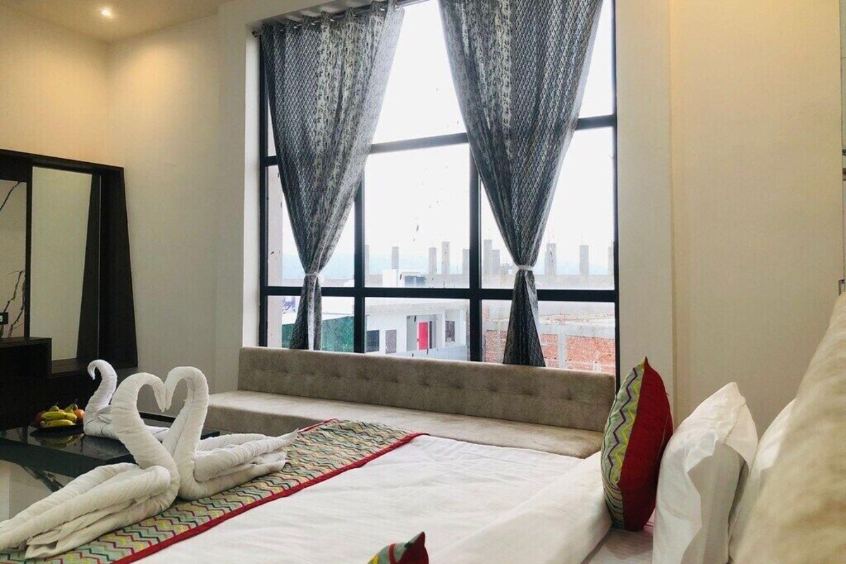 A hotel room with a bed, a view of the city through large windows, and a decorative swan towel arrangement.