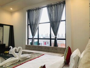 A hotel room with a bed, a view of the city through large windows, and a decorative swan towel arrangement. - jss .inn pushkar (Ajmer)