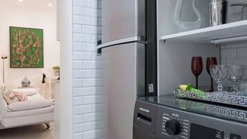 Una cocina moderna con lavadora integrada, pared de ladrillo blanco y zona de comedor con sofá y mesa.