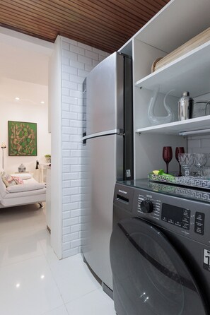 A modern kitchen with a built-in washing machine, white brick wall, and a dining area with a sofa and table. - Copacabana Beach Apartment (Rio de Janeiro)