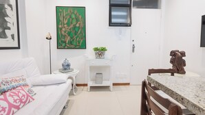 En moderne stue med en hvid sofa, et sofabord, et spisebord med stole, et lille sofabord med en plante og billeder på væggene.