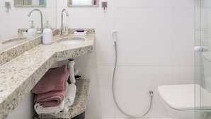Et moderne badeværelse med bordplade i granit, glasvæg omkring brusenichen og et hvidt toilet.