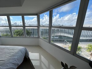 Ein Schlafzimmer mit großem Fenster, einem Bett und Blick auf eine Stadtlandschaft.