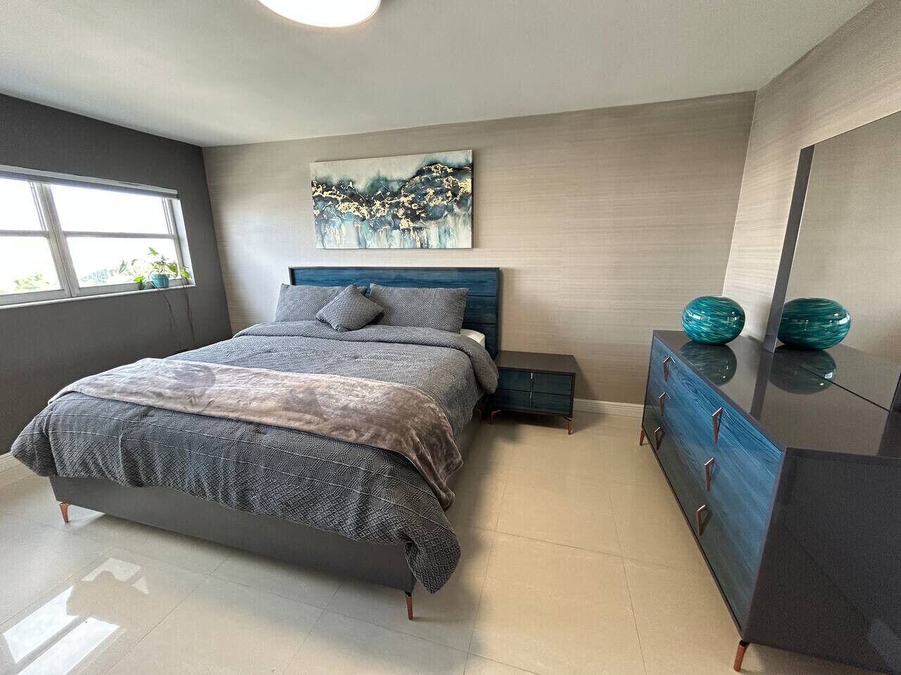 Un dormitorio con cama, mesitas de noche, cómoda y un cuadro en la pared.