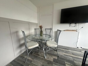 A dining area with a glass table, four chairs, a vase with dried flowers, and a mounted TV on the wall. - Central Wimbledon Apartment With 2 Bedrooms, Free Parking, Fast Wifi (London)