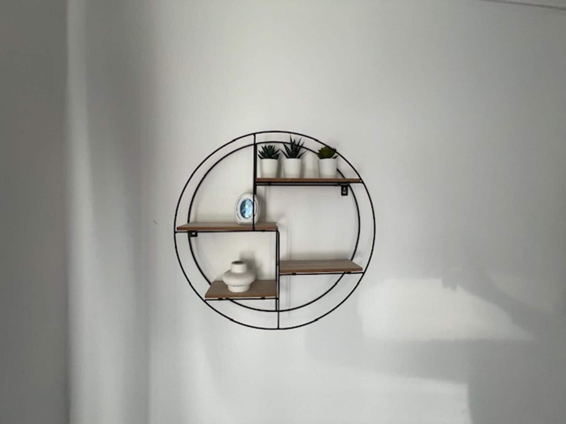 A circular wall-mounted shelf unit with multiple compartments, each holding a potted plant and a small decorative item.