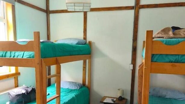 Una habitació amb llits superposats, una taula petita, una làmpada penjant i una catifes al terra.