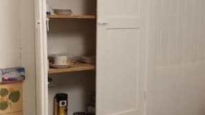 Un armari blanc amb una porta oberta a mig fer, on es veuen prateleires a l'interior.