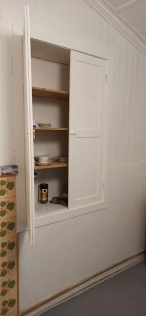 Une armoire blanche, dont la porte est entrouverte, laissant entrevoir des étagères à l’intérieur.