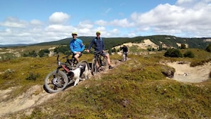 Un grup de persones en un sender de bicicleta de muntanya amb un cel clar i un paisatge amb turons al fons.