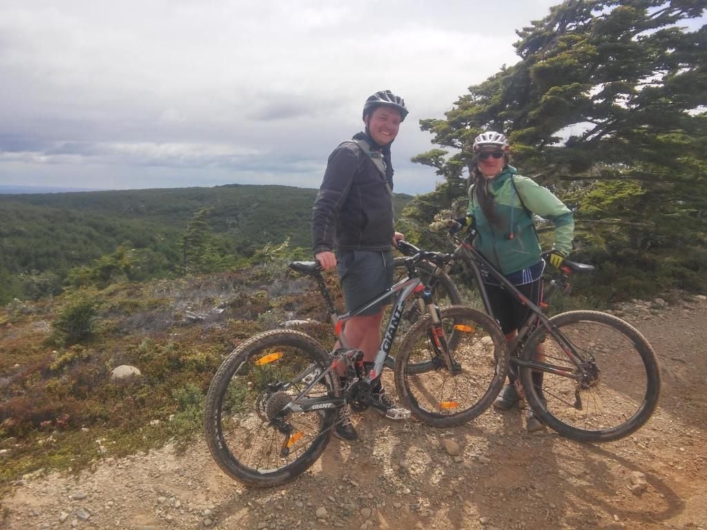 Dos personas de pie en un sendero de tierra con bicicletas, en un entorno natural.