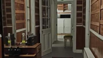Un pasillo estrecho con paredes de madera, un tapete, un espejo y una puerta que da a otra habitación.