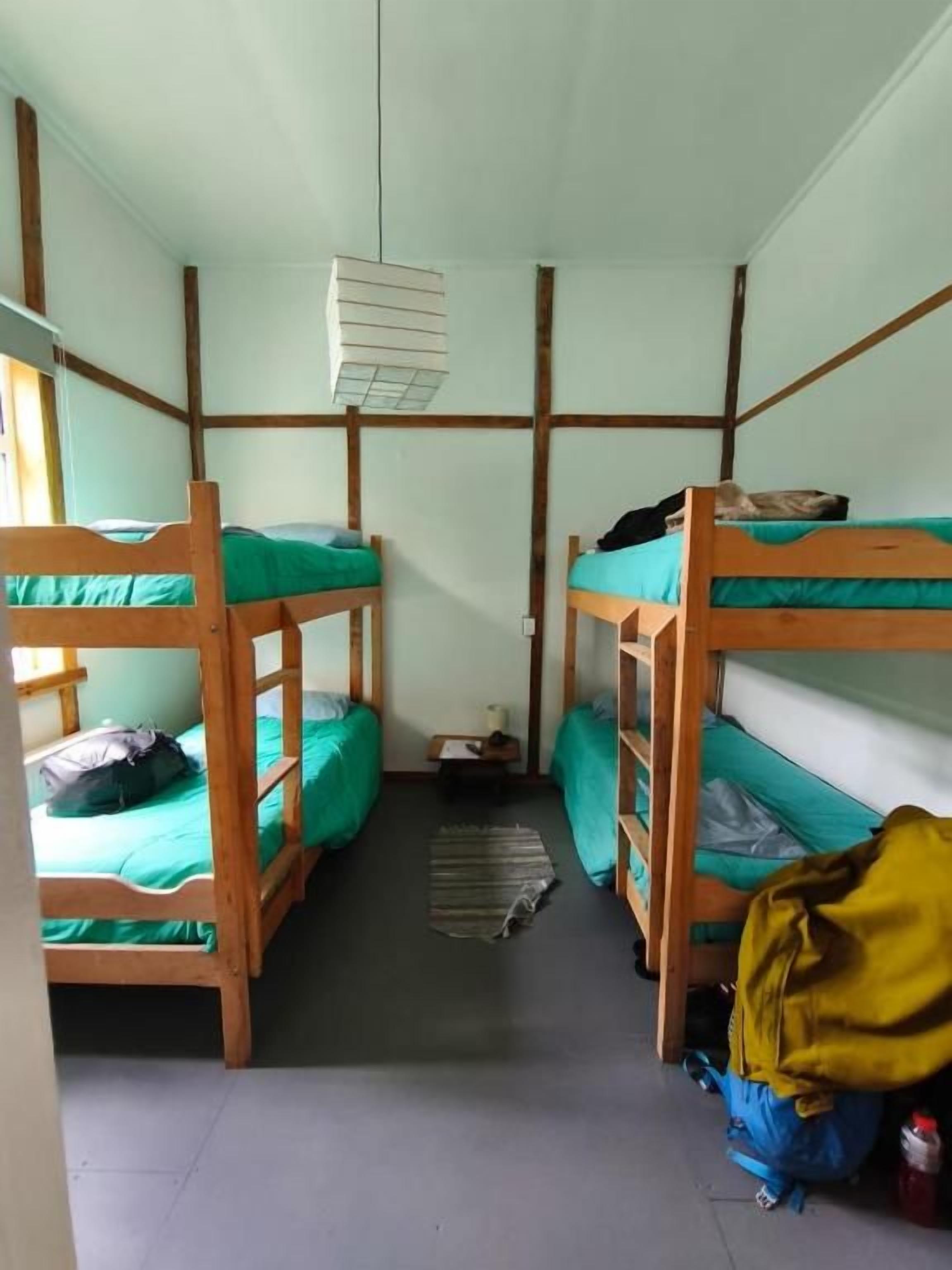 Une chambre de dortoir avec des lits superposés, une petite table et un luminaire suspendu.
