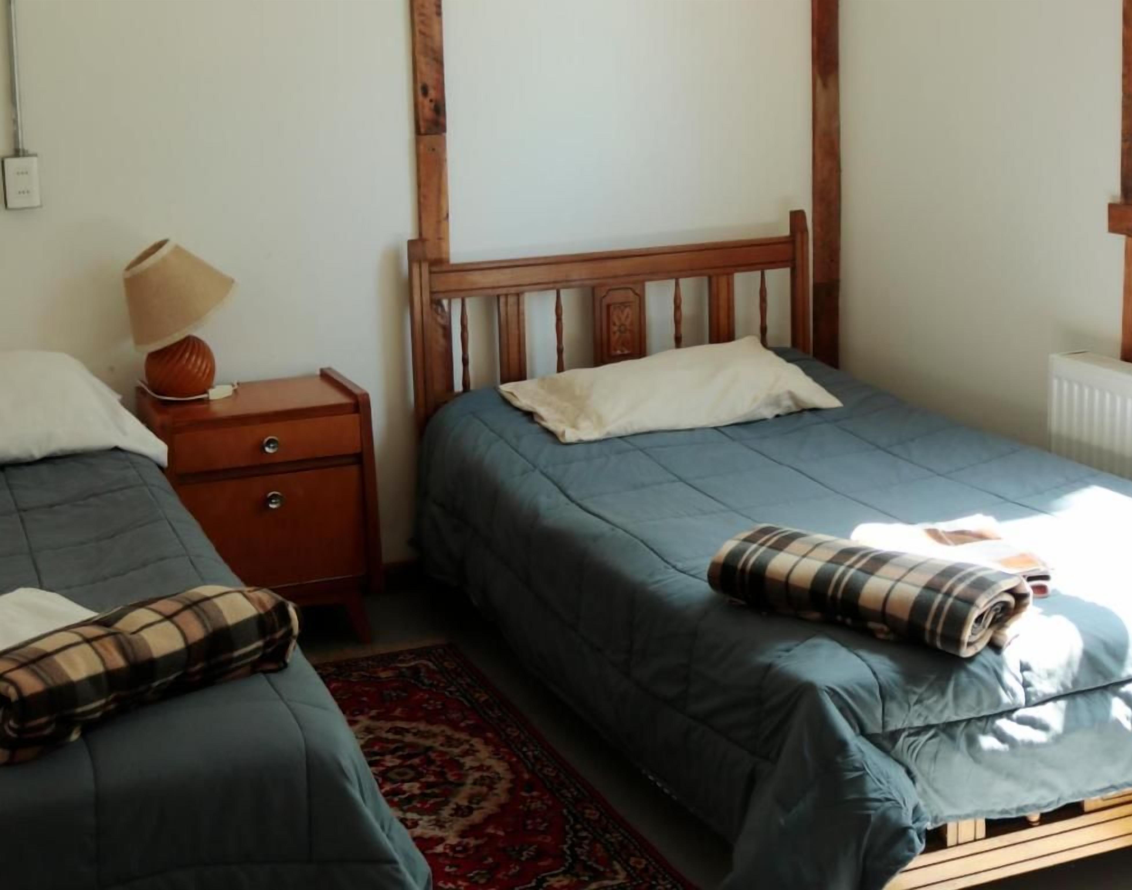 A bedroom with two single beds, a nightstand with a lamp, and a red patterned rug.
