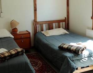 A bedroom with two single beds, a nightstand with a lamp, and a red patterned rug. - Casa Bike (Punta Arenas)