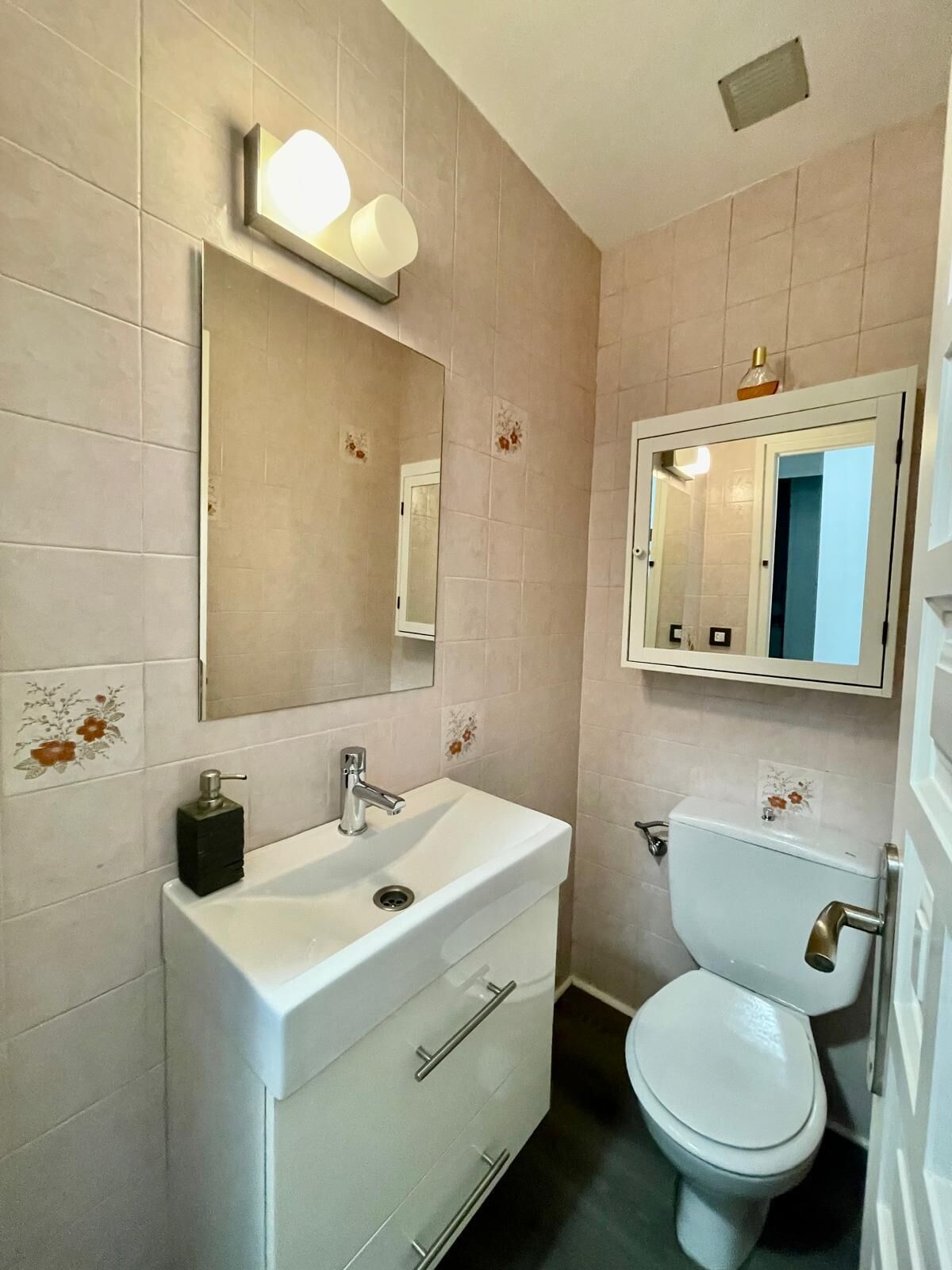 A bathroom with a white sink, a mirror, a toilet, and a light fixture above the mirror.
