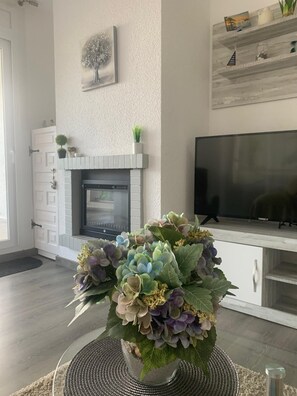A living room with a fireplace, a television, and a decorative plant arrangement. - Charming apartment with views of the sea and mountains (Roses)