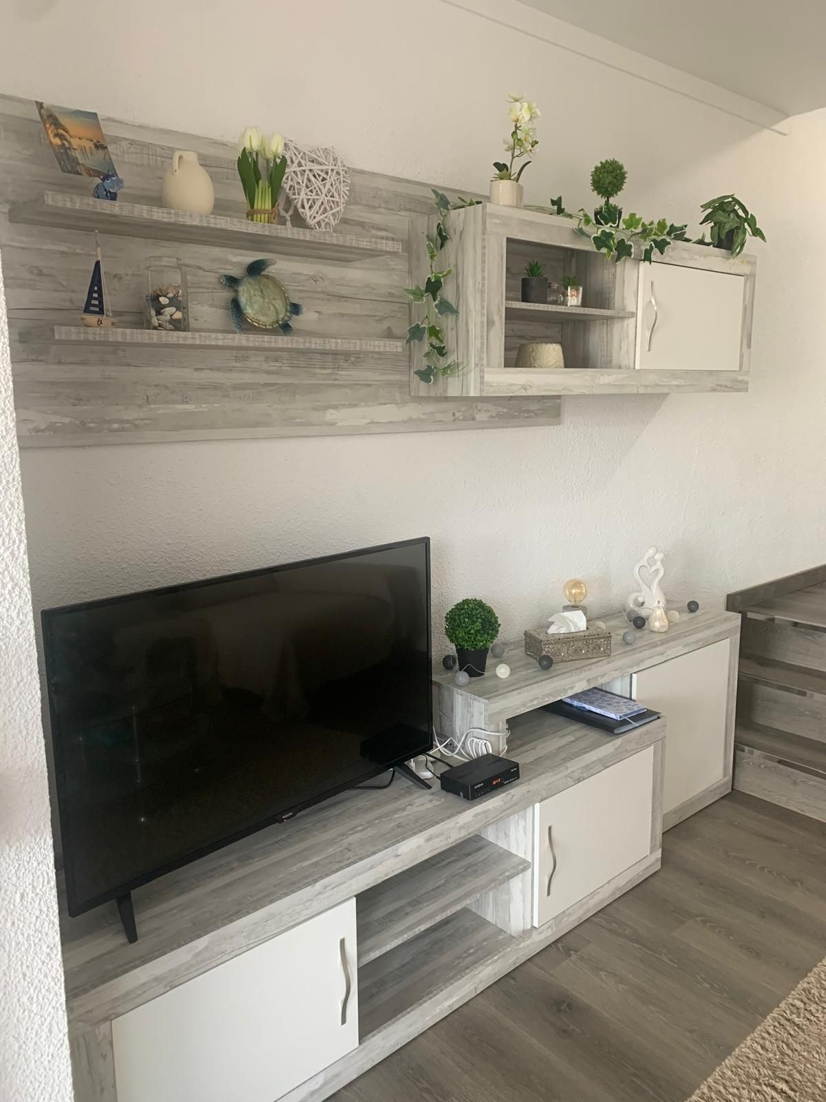 Ein Wohnzimmer mit Flachbildfernseher, Holzregalen mit Dekoration und einer Einbauschränken.